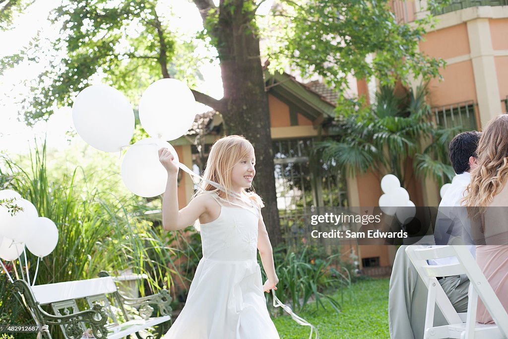 Young girl at outdoor party holding balloons smiling with people in background