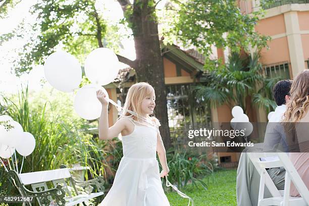 Young Girl At Outdoor Party Holding Balloons Smiling With People In Background, Bildbanksbilder