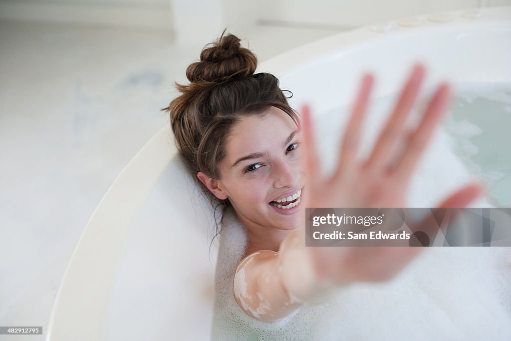 Woman relaxing in bubble bath hiding behind hand and smiling