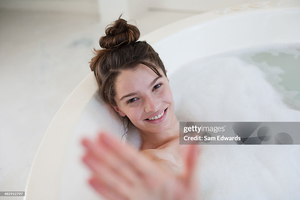 Mulher relaxante no banho de espuma que s'escondem atrás de mão e sorrir