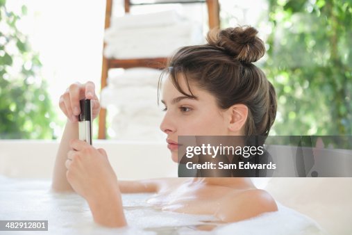 Woman relaxing in bubble bath using cellular phone Woman relaxing in bubble bath using cellular phone