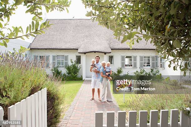 man and woman holding babies in front of house with sold sign and white fence - family of four in front of house stock pictures, royalty-free photos & images