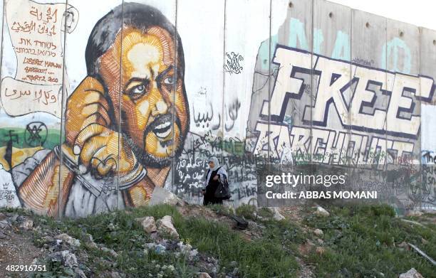 Palestinian woman walks past a graffiti-covered section of the controversial Israeli separation wall showing jailed Fatah leader Marwan Barghuti at...