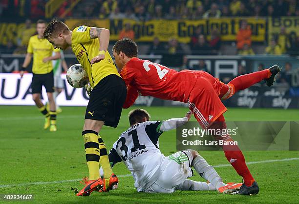 Marco Reus of Dortmund challenges goalkeeper Max Gruen and Robin Knoche of Wolfsburg on his way to score his teams second goal during the Bundesliga...