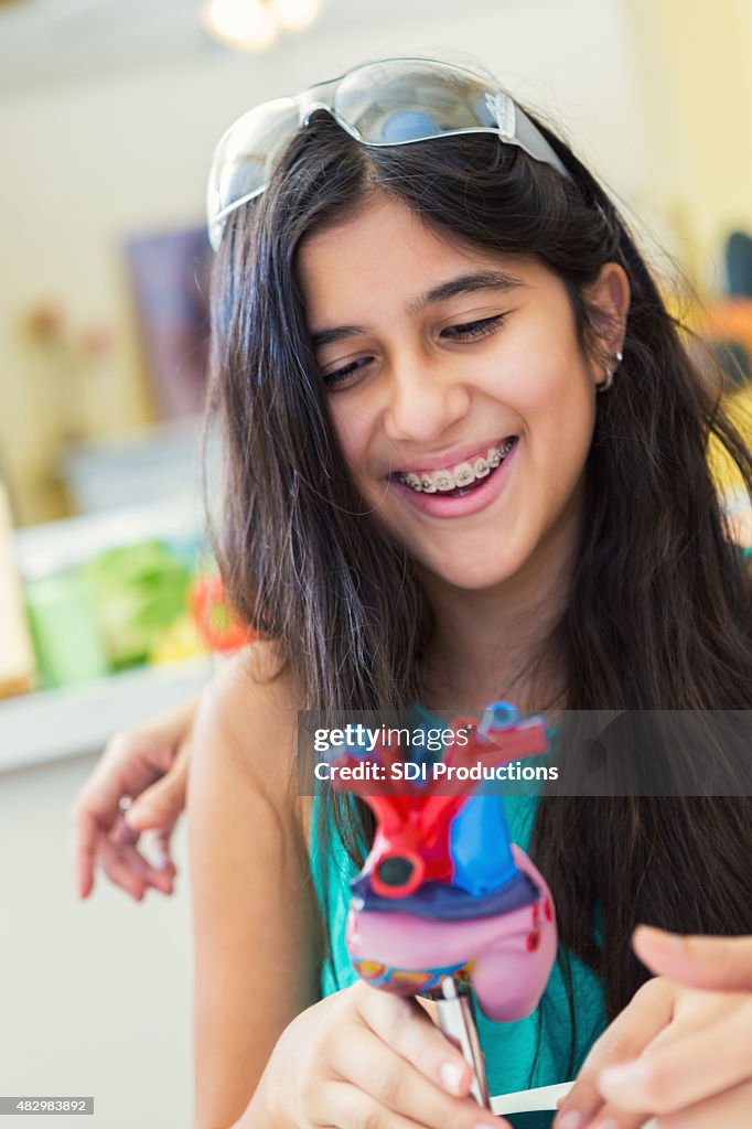 Happy preteen girl studying heart model during homeschool science class