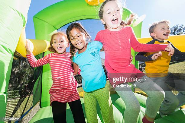 vier multikulturellen kinder springen auf der hüpfburg - bouncy castle stock-fotos und bilder