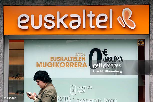 Pedestrian uses a smartphone as she walks past a Euskaltel SA phone store in Barakaldo, Spain, on Tuesday, Aug. 4., 2015. Euskaltel, the phone and...