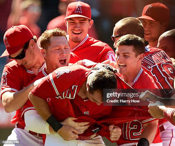 Taylor Featherston of the Los Angeles Angels is mobbed by Kole Calhoun and Johnny Giavotella in response to his run from a wild pitch during the...