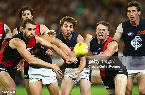 Dale Thomas of the Blues handballs whilst being tackled by Jobe Watson and Brendon Goddard of the Bombers during the round three AFL match between...