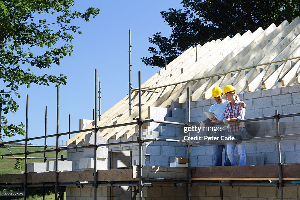 Couple looking at tablet at unfinished house biuld