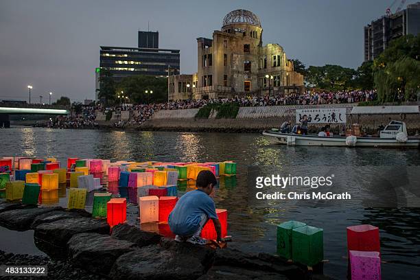 Boy floats a candle lit paper lantern on the river in front of the Atomic Bomb Dome during 70th anniversary activities, commemorating the atomic...