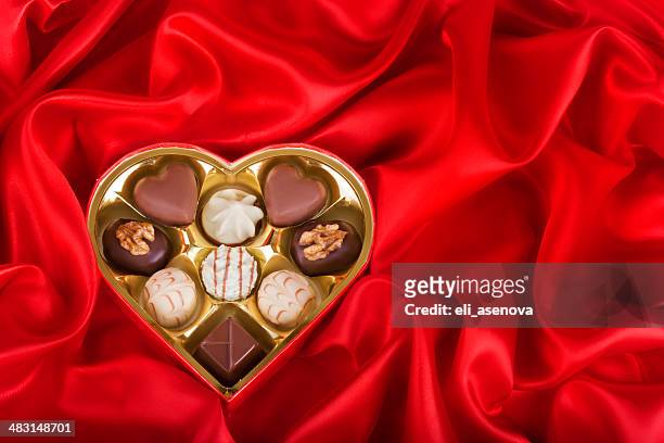 heart shaped box of candy on red satin background - chocolate box stockfoto's en -beelden
