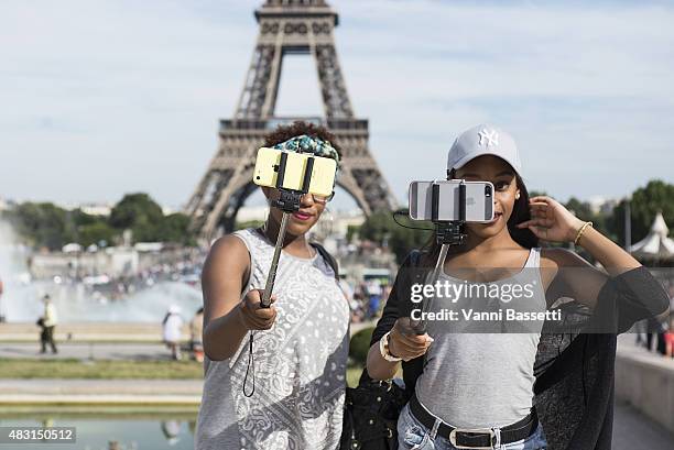 Tourists take a selfie using a selfie stick in front of the Eiffel Tower on August 6, 2015 in Paris, France. Using a selfie stick has become a more...