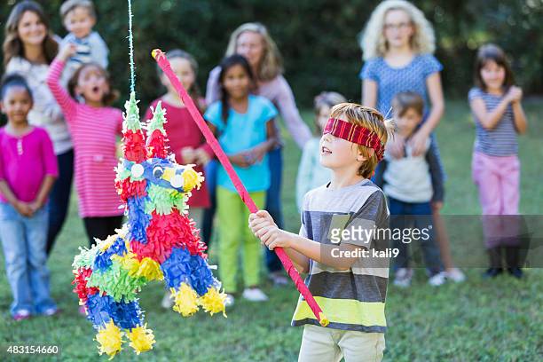 multi-ethnischen gruppe von kindern mit jungen schlagen piñata - pinata stock-fotos und bilder