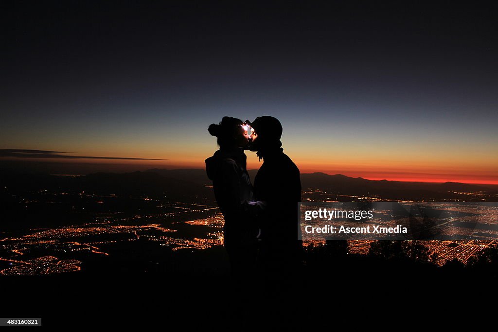 Couple wearing headlamps kiss above city lights