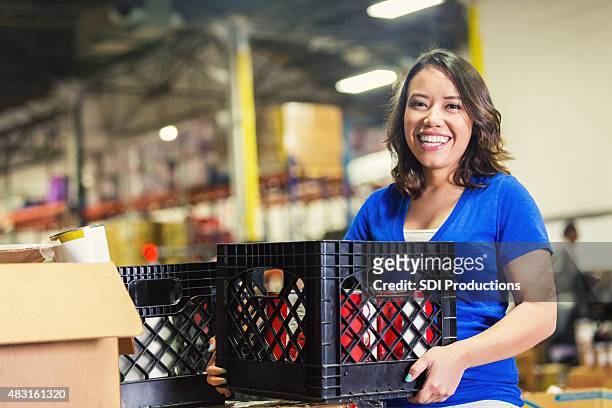 young asian american volunteer working in food bank warehouse - charitable donation stock pictures, royalty-free photos & images
