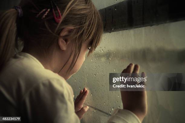 lonely child looking through window - abused girl stock pictures, royalty-free photos & images