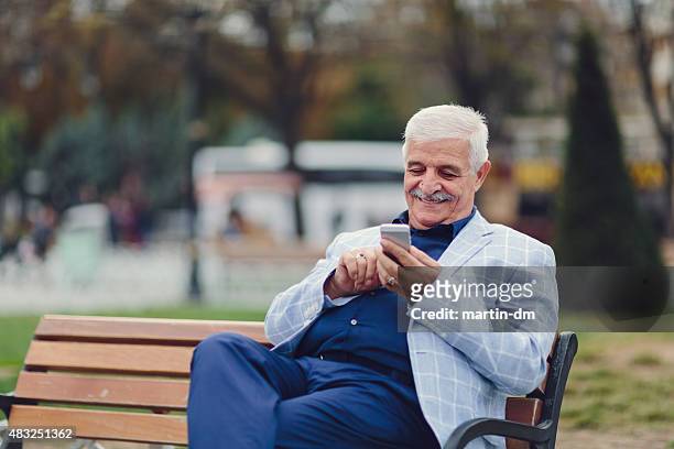 uomo anziano seduto sulla panchina e usa uno smartphone - contemporary istanbul foto e immagini stock