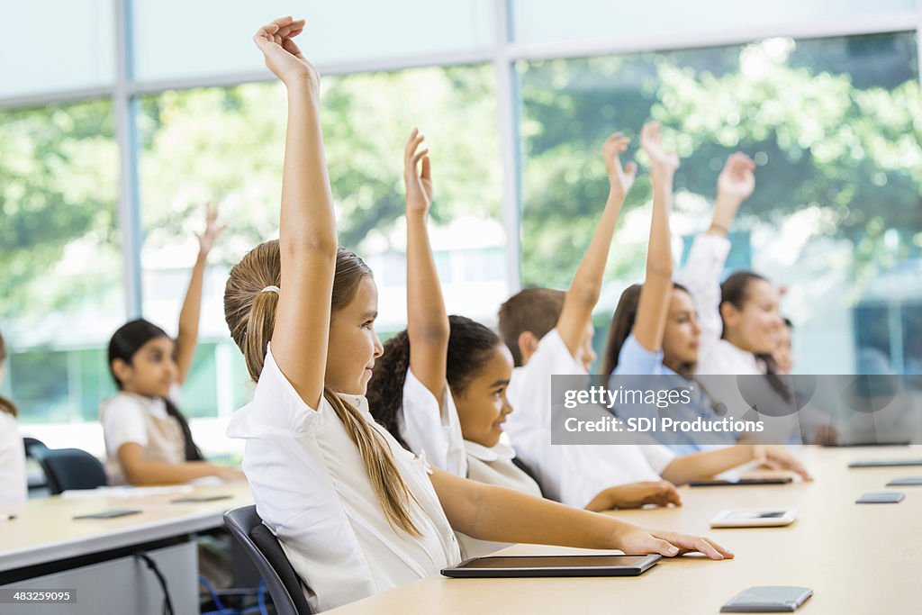 Private elementary school students raising hands to answer teacher's question