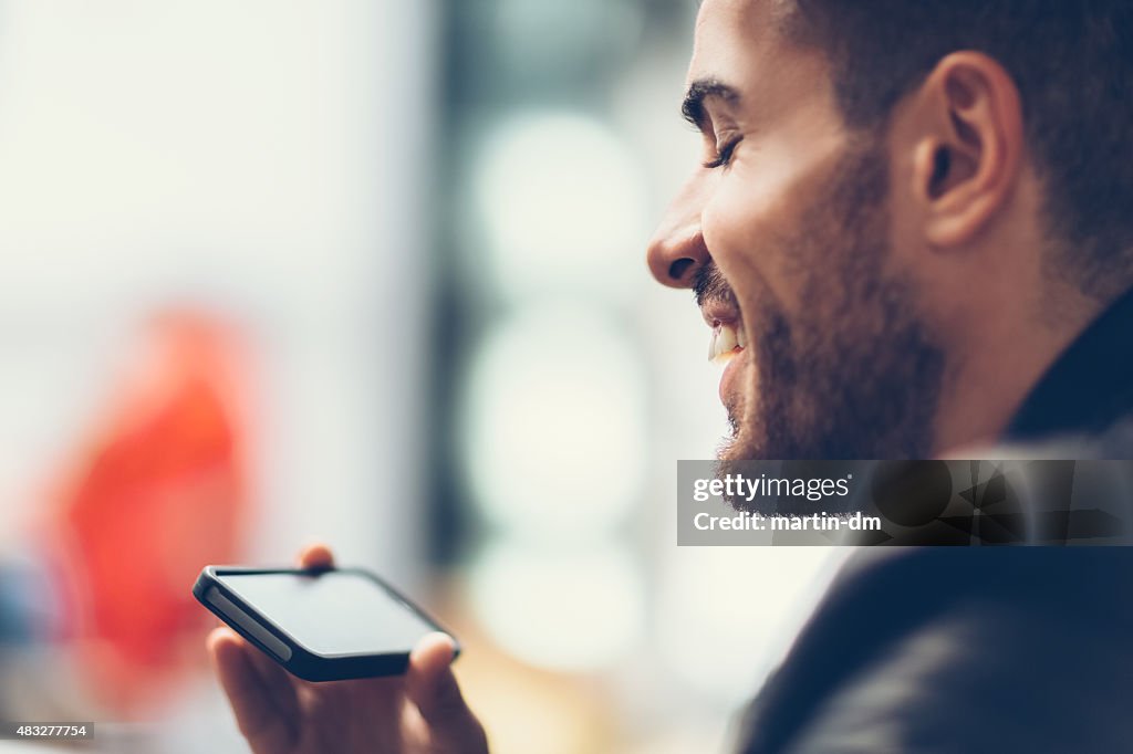 Lächelnder Mann, mit smartphone vor dem Fernseher