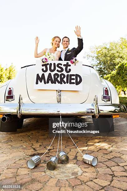 recién casados agitando a convertible car con bidones de adjunto - newlywed fotografías e imágenes de stock