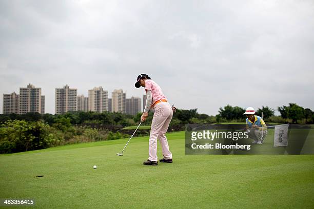 Caddie looks on as a golfer hits a ball towards the cup on the green at Mission Hills Resort Haikou in Haikou, Hainan Province, China, on Saturday,...