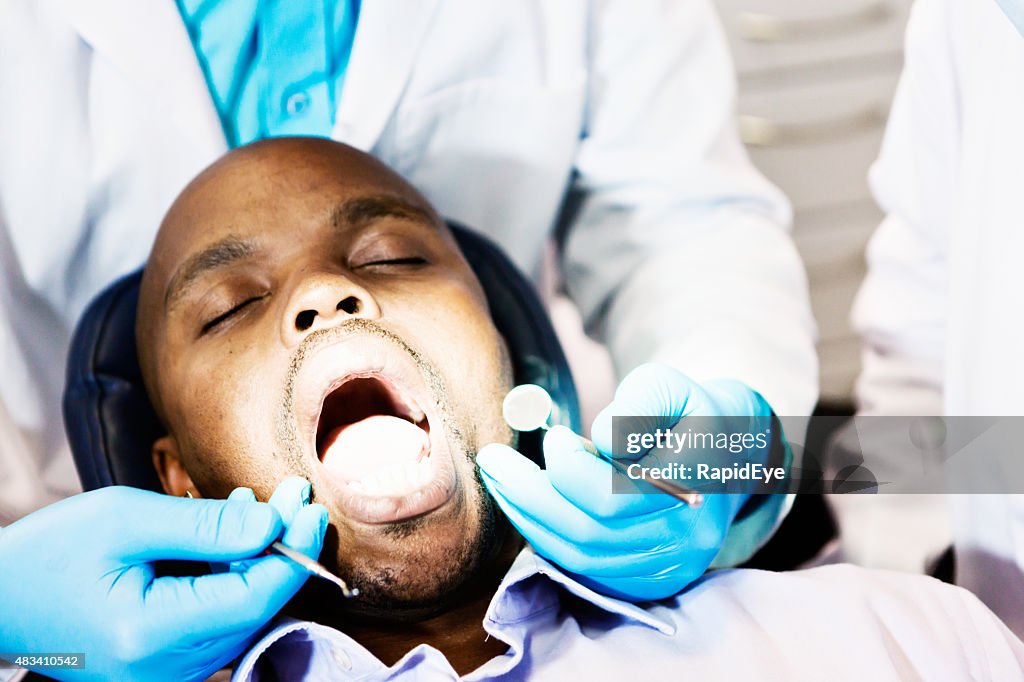 Dentist holds dental probe and mirror by patient's open mouth