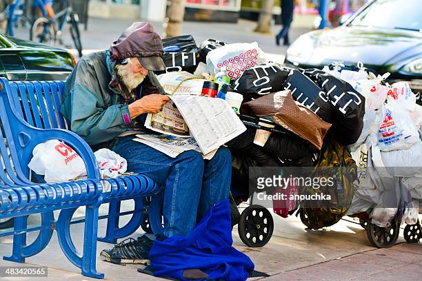 homeless senior man sitting on bench, reading newspaper - homeless los angeles stock pictures, royalty-free photos & images