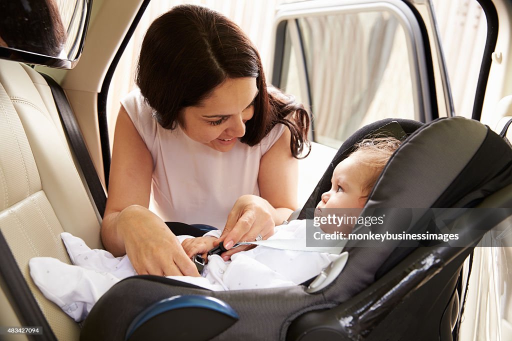 Mother Putting Baby Son Into Car Travel Seat
