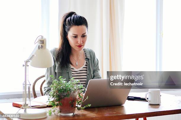 young brunette blick auf laptop - brunette sitting at desk stock-fotos und bilder