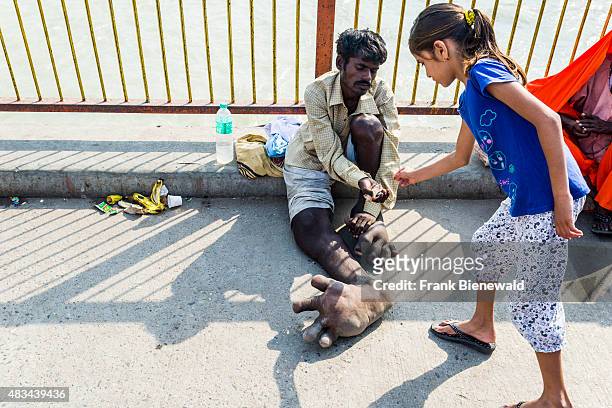 Beggar with Elephantiasis at his feet is receiving some money from a girl at Harki Pauri Ghat at the holy river Ganges.