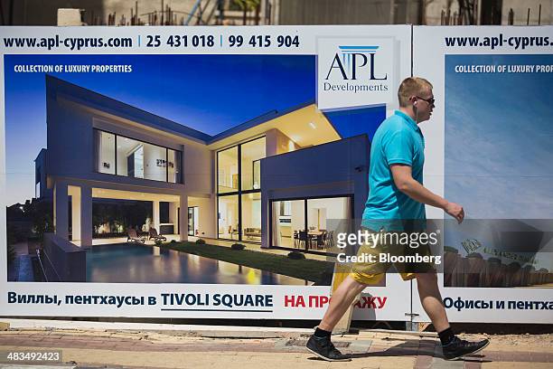 Tourist passes a billboard by the APL Group, advertising luxury property for sale in Russian cyrillic script in Limassol, Cyprus, on Tuesday, April...