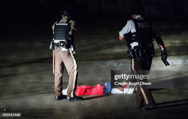 Police stand over a man with gunshot wounds lying in a parking lot after a shoot out with police along West Florissant Street during a demonstration...