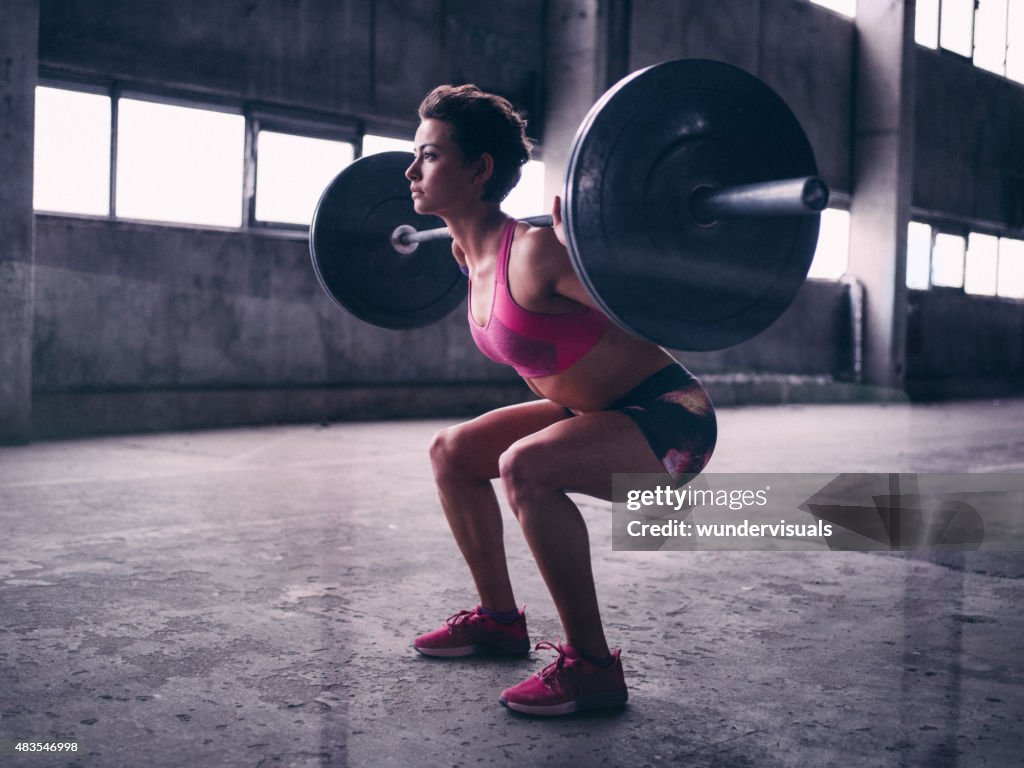 Young woman resting a heavy barbell on her shoulders