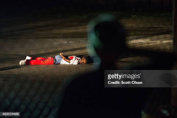 Young boy looks at a man with gunshot wounds lying in a parking lot after a shoot out with police along West Florissant Street during a demonstration...