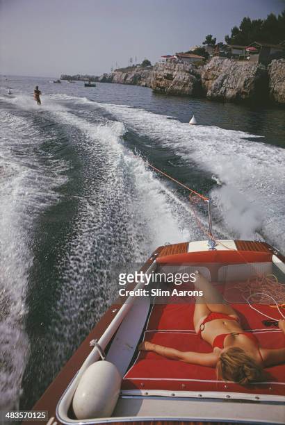 Woman sunbathing in a motorboat as it tows a waterskiier, in the sea off the Hotel du Cap-Eden-Roc in Antibes on the French Riviera, August 1969.