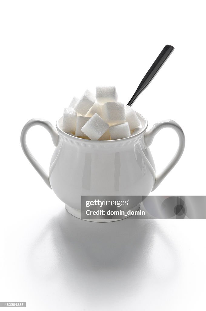 Sugar bowl full of sugar cubes and spoon, isolated on white