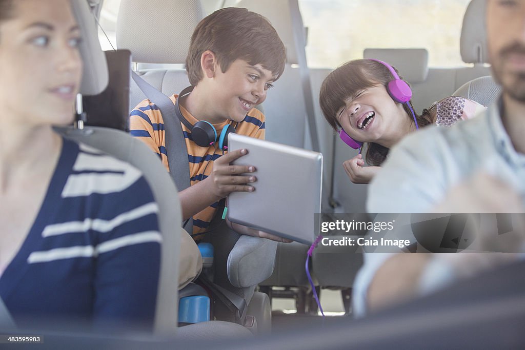 Happy brother and sister using digital tablet in back seat of car