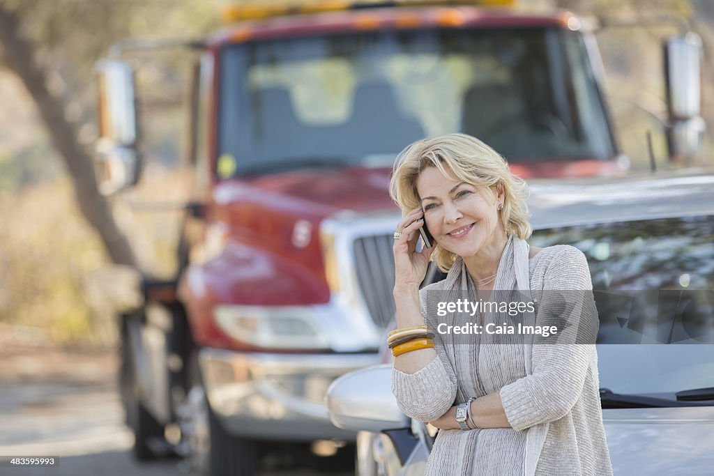 Woman talking on cell phone near tow truck at roadside