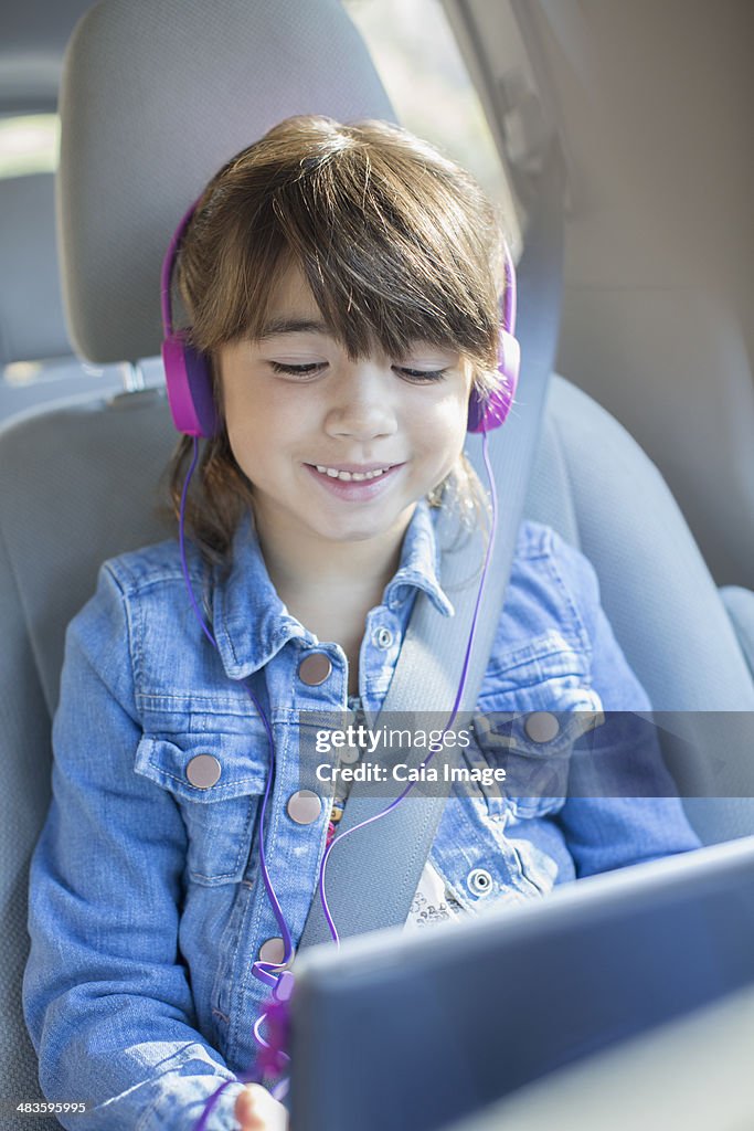 Happy girl with headphones using digital tablet in car