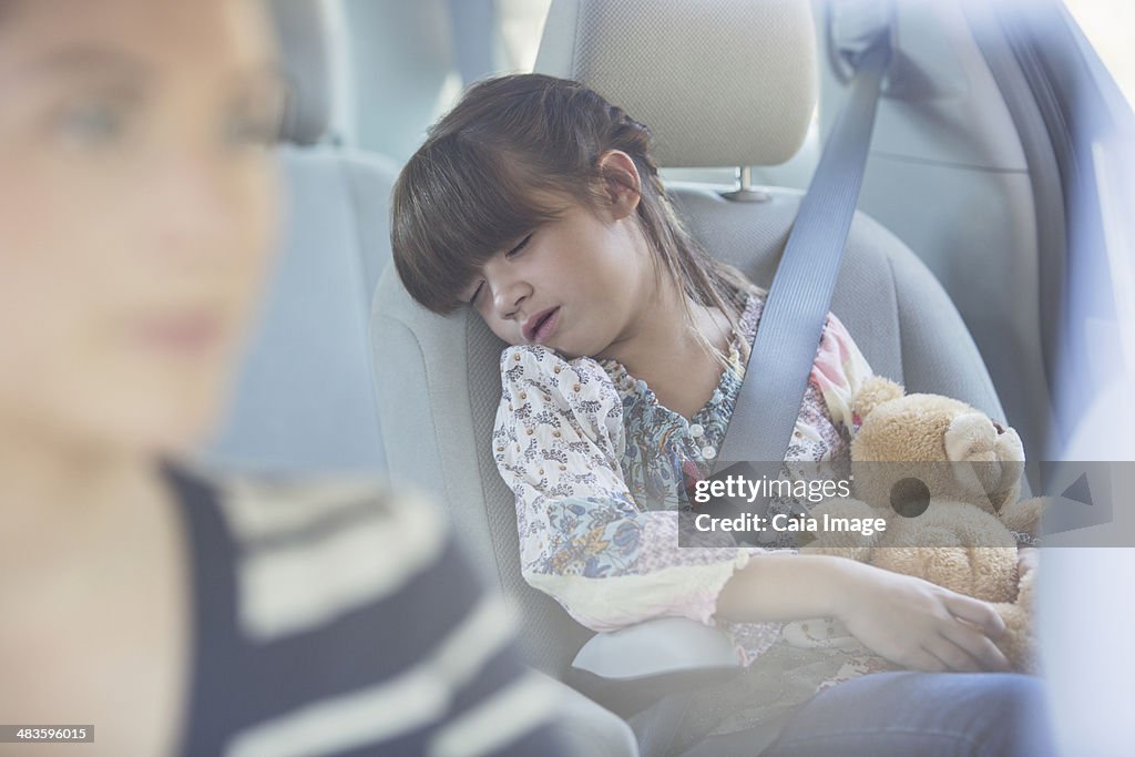 Girl with teddy bear sleeping in back seat of car