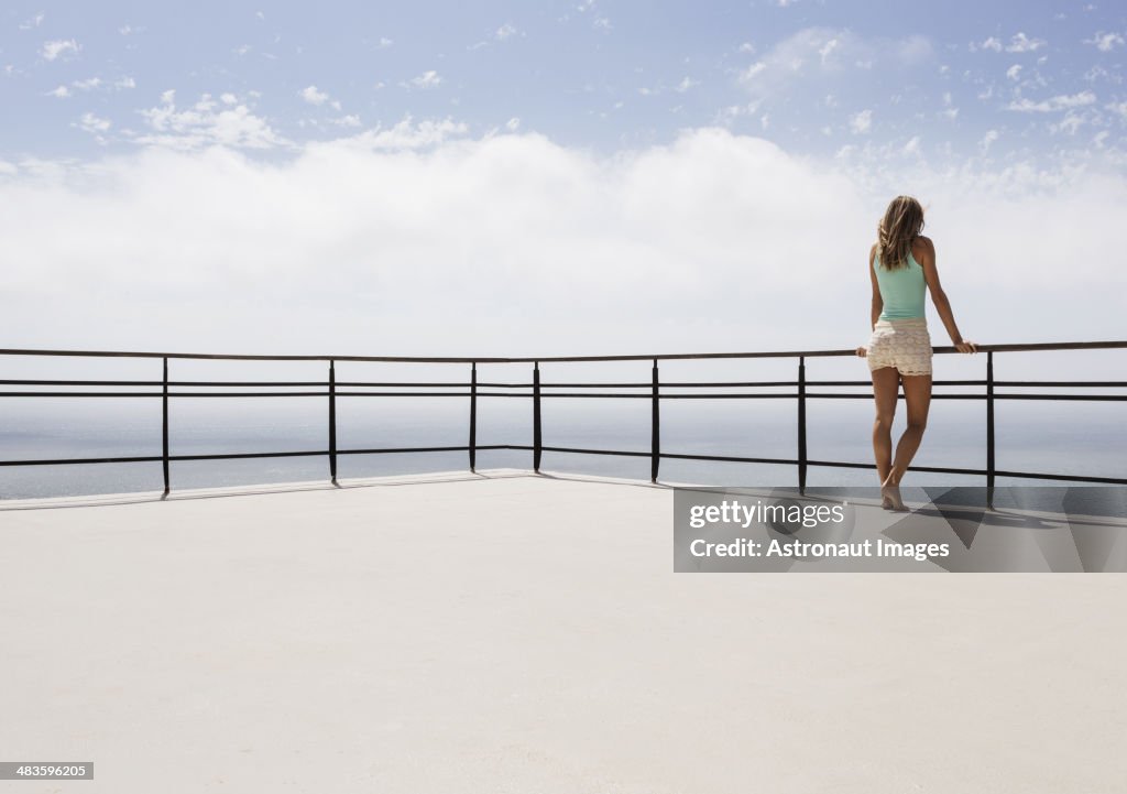 Mulher em pé na sacada com vista para o mar