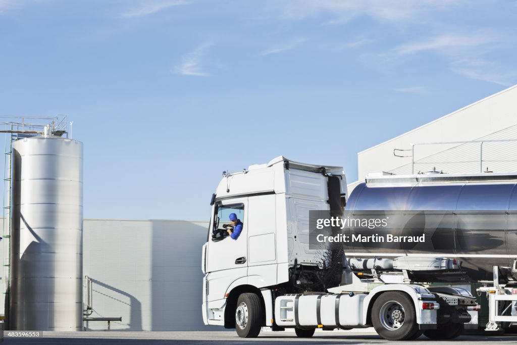 Truck driver parking stainless steel milk tanker outside silage storage tower