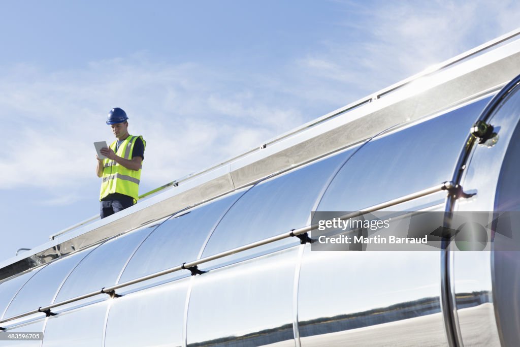 Worker using digital tablet on platform above stainless steel milk tanker