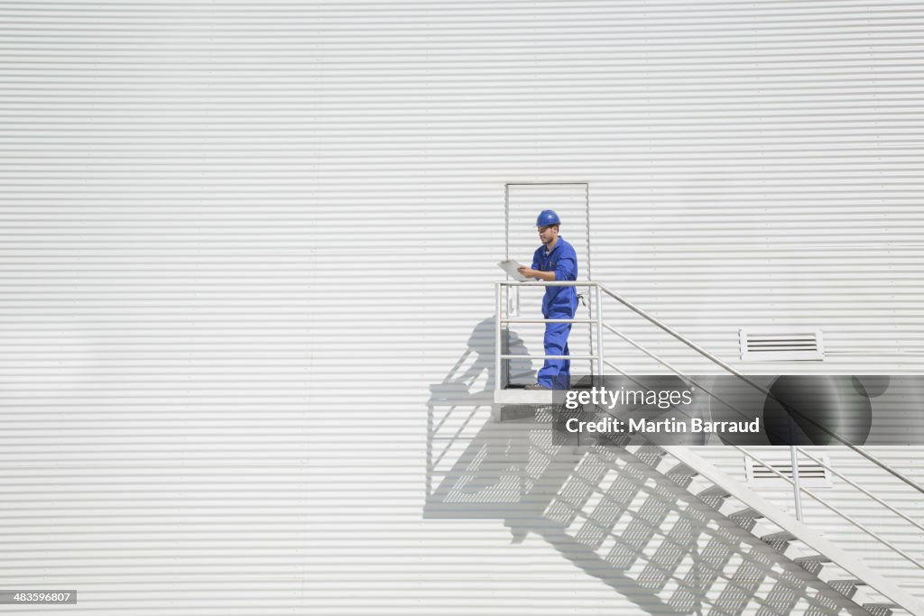 Worker with clipboard on stairs along building