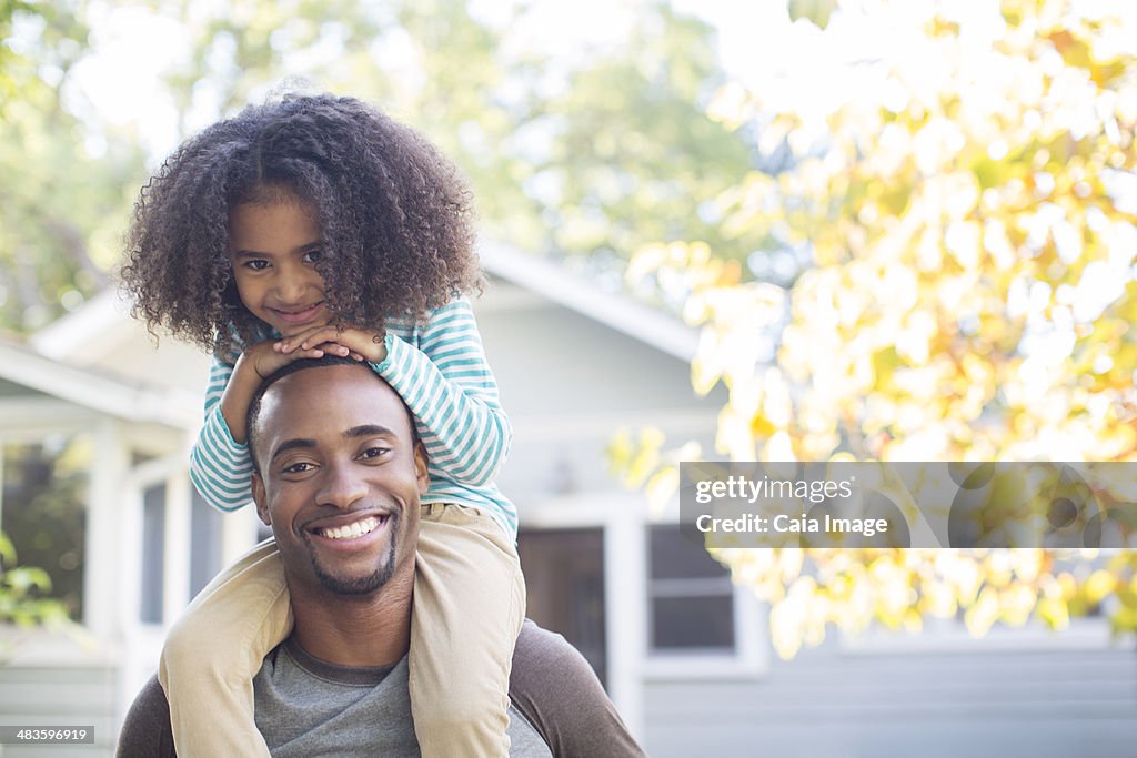 Portrait of happy father carrying daughter on shoulders