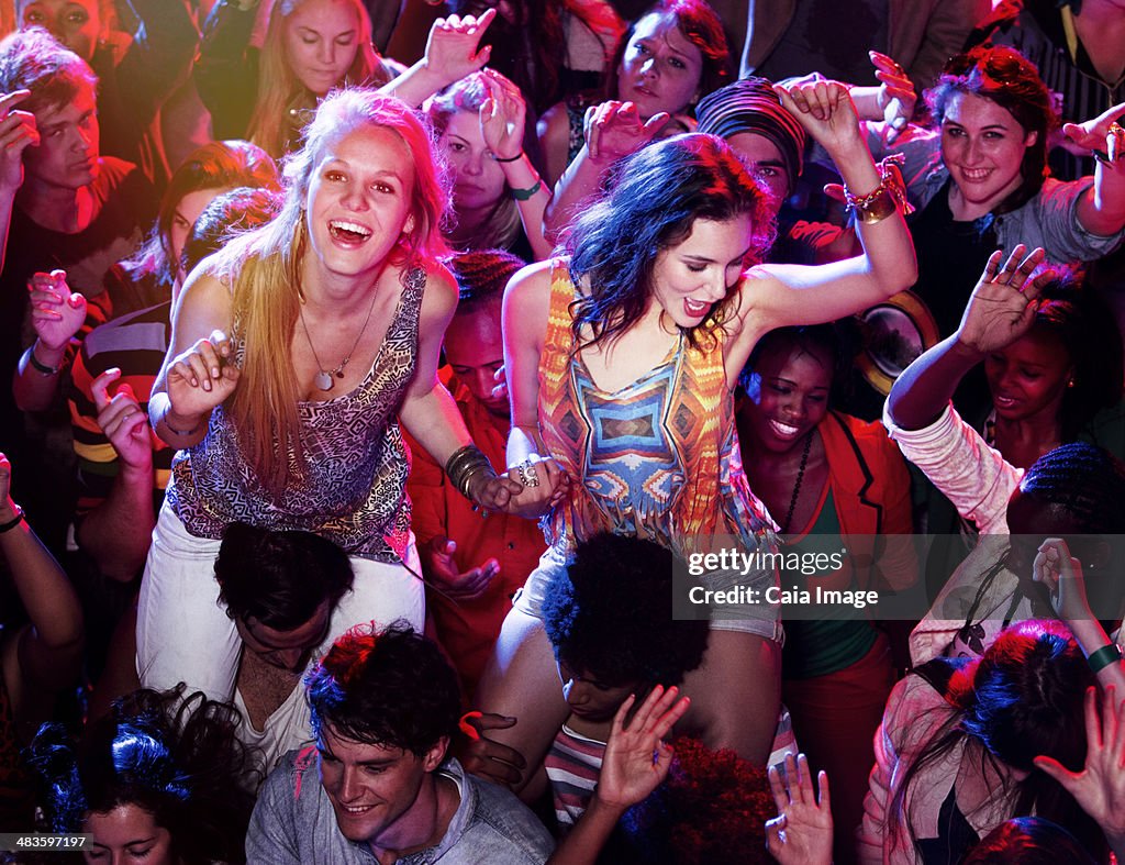 Men carrying cheering women on shoulders in crowd at music festival