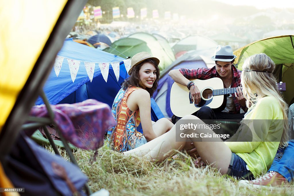 Friends with guitar hanging out near tents at music festival