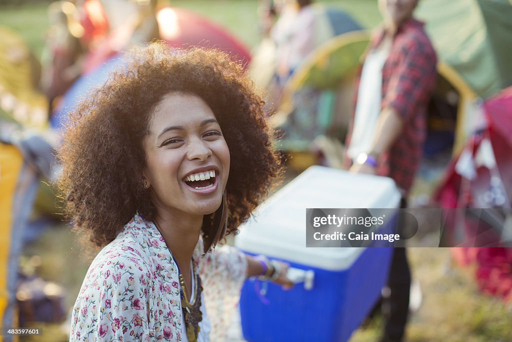 Portrait of laughing woman helping man carry cooler outside tents at music festival