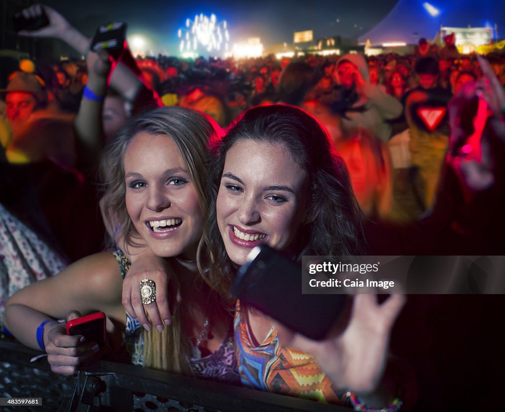 Friends taking self-portrait with camera phone at music festival
